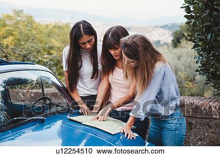 Stock Image - Friends reading route map on car bonnet in countryside. Fotosearch