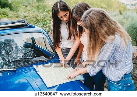 Stock Photo - Friends reading route map on car bonnet in countryside. Fotosearch