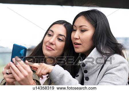 Friends reading text message on smartphone in street View Large Photo Image Stock Photo - Friends reading text message on smartphone in street. Fotosearch