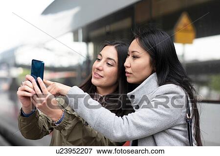Stock Photo - Friends reading text message on smartphone in street. Fotosearch