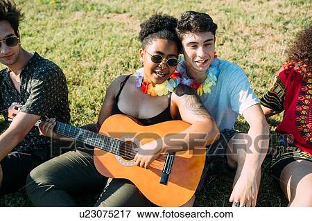 Friends relaxing, playing guitar in park View Large Photo Image Stock Photo - Friends relaxing, playing guitar in park. Fotosearch