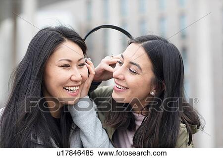 Stock Photography - Friends sharing headphone, listening to music in city. Fotosearch