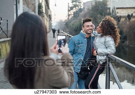 Stock Image - Friends taking photograph by river, Milano, Lombardia, Italy. Fotosearch