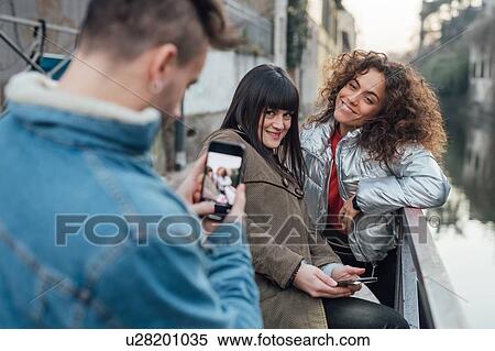 Stock Photography - Friends taking photograph by river, Milano, Lombardia, Italy. Fotosearch