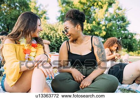 Stock Image - Friends talking at picnic in park. Fotosearch