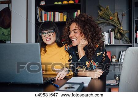 Stock Photo - Friends using laptop in home office. Fotosearch