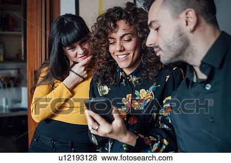 Friends using smartphone at home View Large Photo Image Stock Photo - Friends using smartphone at home. Fotosearch