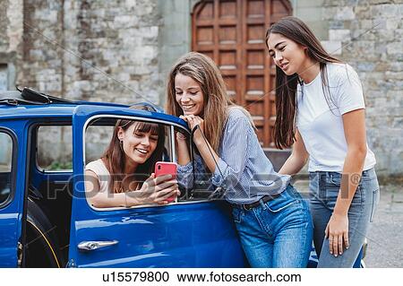 Stock Image - Friends using smartphone beside car. Fotosearch
