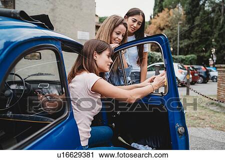 Friends using smartphone beside car View Large Photo Image Stock Image - Friends using smartphone beside car. Fotosearch