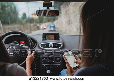 Stock Image - Friends using smartphone inside car. Fotosearch