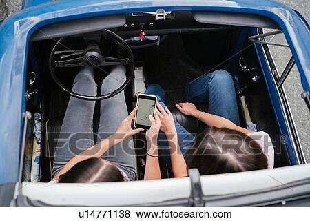 Stock Photo - Friends using smartphone inside car. Fotosearch