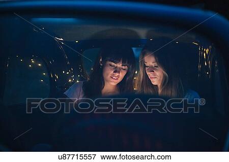 Stock Photo - Friends using smartphone inside car. Fotosearch