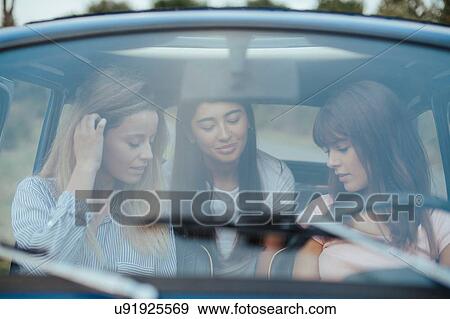 Stock Photo - Friends using smartphone inside car. Fotosearch