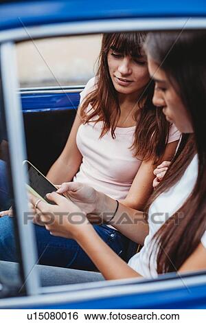 Stock Photograph - Friends using smartphone inside car. Fotosearch