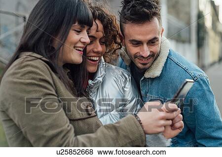Friends using smartphone on pavement View Large Photo Image Stock Photo - Friends using smartphone on pavement. Fotosearch
