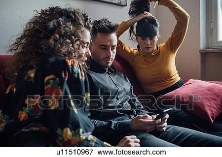 Stock Photo - Friends using smartphone on sofa. Fotosearch