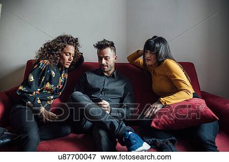Stock Photo - Friends using smartphone on sofa. Fotosearch