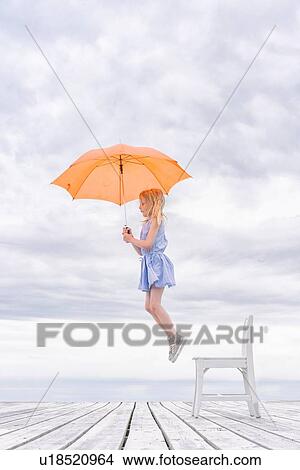 Picture - Girl being lifted off her chair by umbrella. Fotosearch