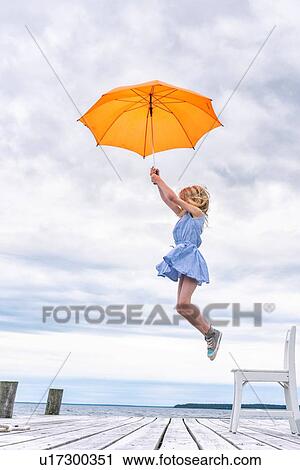 Stock Image - Girl being lifted off her chair by umbrella. Fotosearch
