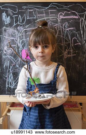 Stock Image - Girl holding stick and feather craft by blackboard. Fotosearch