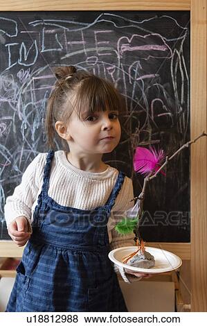 Stock Photo - Girl holding stick and feather craft by blackboard. Fotosearch