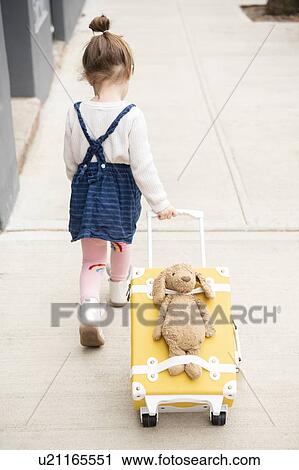 Stock Image - Girl pulling suitcase with teddy bear strapped to it. Fotosearch