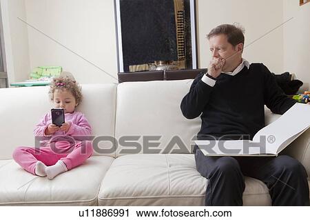 Girl using smart phone as her father reads book View Large Photo Image Stock Image - Girl using smart phone as her father reads book. Fotosearch