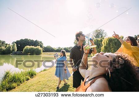 Stock Image - Group of friends blowing bubbles in park. Fotosearch