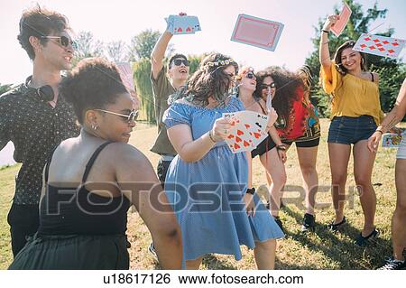 Stock Photograph - Group of friends dancing, throwing playing cards into air in park. Fotosearch