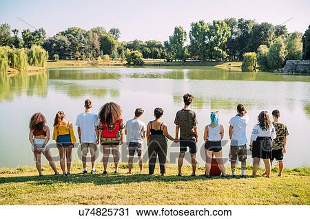 Stock Image - Group of friends enjoying view of lake in park. Fotosearch