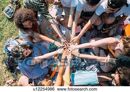 Stock Photograph - Group of friends overlapping hands in circle in park. Fotosearch