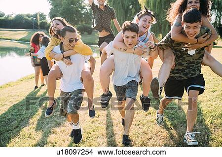 Picture - Group of friends piggyback racing in park. Fotosearch