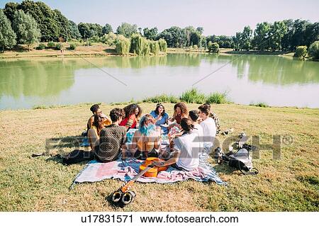Stock Image - Group of friends relaxing at picnic in park. Fotosearch