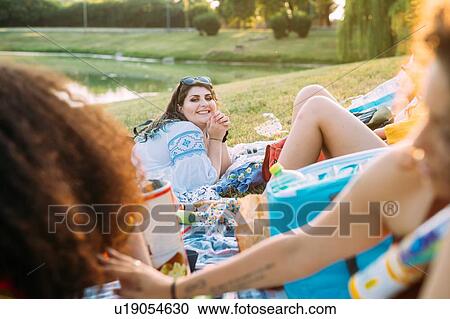 Stock Image - Group of friends relaxing at picnic in park. Fotosearch