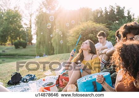 Stock Photograph - Group of friends relaxing, blowing bubbles at picnic in park. Fotosearch