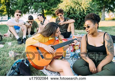 Group of friends relaxing, playing guitar at picnic in park View Large Photo Image Picture - Group of friends relaxing, playing guitar at picnic in park. Fotosearch