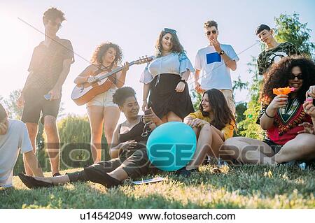 Stock Photo - Group of friends relaxing, playing guitar at picnic in park. Fotosearch