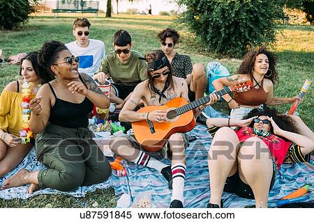 Stock Photography - Group of friends relaxing, playing guitar at picnic in park. Fotosearch