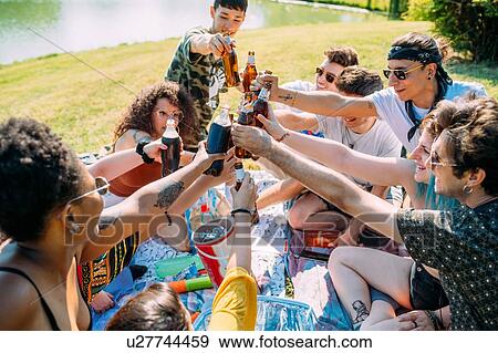 Group of friends relaxing, toasting soft drinks at picnic in park View Large Photo Image Stock Photo - Group of friends relaxing, toasting soft drinks at picnic in park. Fotosearch