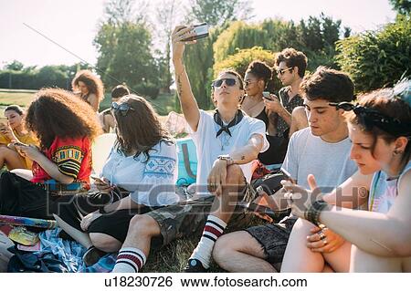 Group of friends relaxing, using smartphone in park View Large Photo Image Stock Photograph - Group of friends relaxing, using smartphone in park. Fotosearch