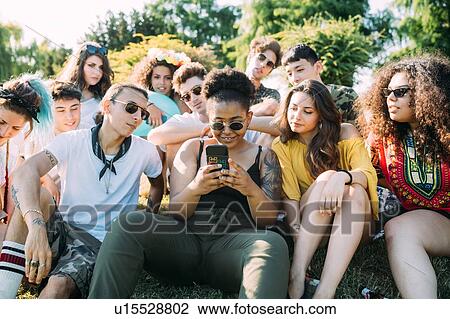 Stock Image - Group of friends using smartphone in park. Fotosearch
