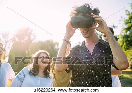 Group of friends watching man looking into VR headset in park View Large Photo Image Picture - Group of friends watching man looking into VR headset in park. Fotosearch