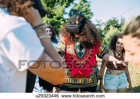 Group of friends watching woman looking into VR headset in park View Large Photo Image Stock Photograph - Group of friends watching woman looking into VR headset in park. Fotosearch