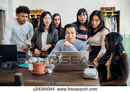 Picture - Group of young businessmen and women looking at laptop in office meeting. Fotosearch