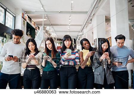 Group of young businesswomen and men in a row, looking at smartphones View Large Photo Image Stock Image - Group of young businesswomen and men in a row, looking at smartphones. Fotosearch