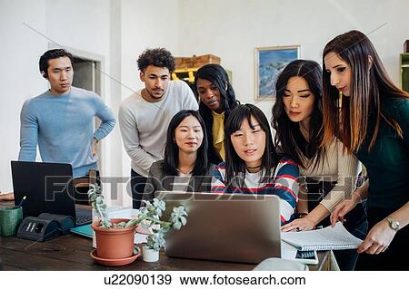 Stock Photo - Group of young businesswomen and men looking at laptop in office meeting. Fotosearch