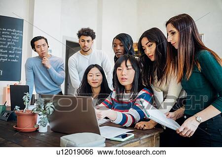 Group of young businesswomen and men looking at laptop in office meeting View Large Photo Image Stock Photograph - Group of young businesswomen and men looking at laptop in office meeting. Fotosearch
