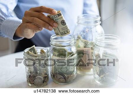Stock Photo - Hand of woman putting money in jar. Fotosearch