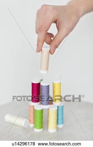Stock Photo - Hand of woman stacking colorful spools of thread. Fotosearch