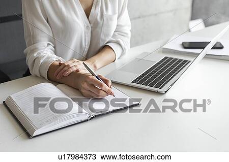 Stock Image - Hand of young businesswoman writing notes at desk. Fotosearch
